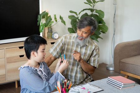 Creative Learning and Family Bonding. A teenage girl engages in art activities with her supportive grandfather.の写真素材