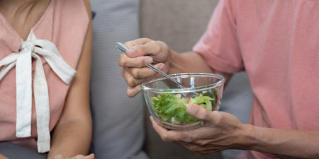 Wellness and Togetherness. Elderly couple feeding each other healthy salad at home.の写真素材