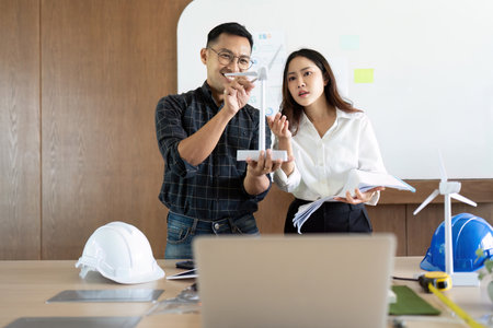Sustainability and Engineering. Engineers presenting eco-friendly building concepts with wind turbine model.の写真素材