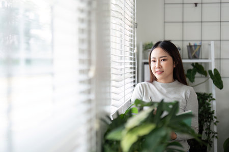 Contemplation and Focus. Young woman reflecting in a bright home office.の写真素材
