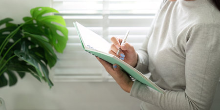 Note Taking and Organization. Woman writing in planner in bright home office.