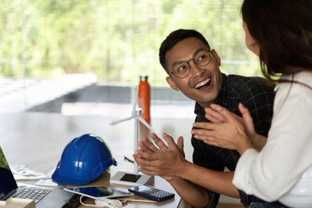 Sustainability and Teamwork. Engineer celebrating success with a colleague in a modern office.
