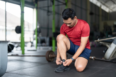 Wellness and Fitness. Man tying shoelaces in gym, preparing for workout.