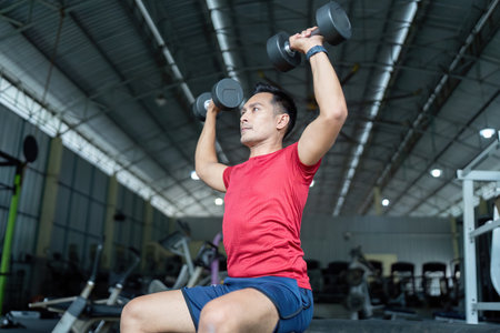 Wellness and Strength Training. Man performing an overhead dumbbell press in the gym.の写真素材