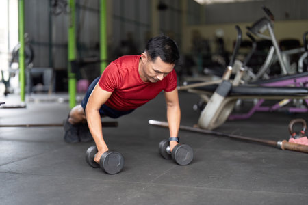 Wellness through Strength Training. Man executing push-up with dumbbells in gym.の写真素材