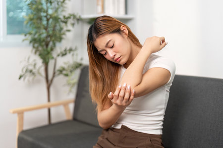 Elbow Pain Management. Young woman rubbing her elbow in discomfort at home.の写真素材