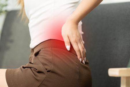 Back Pain Relief. Woman experiencing discomfort in lower back while sitting on sofa.