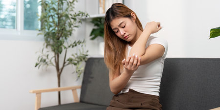 Elbow Pain and Discomfort. Young woman rubbing her elbow in pain at home.