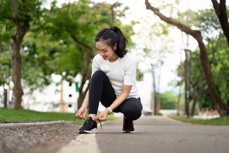 Active Lifestyle. Young woman tying shoelaces before running outdoors in a park.の写真素材