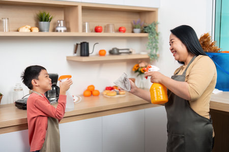 Cleaning Supplies and Family Fun. A mother handing cleaning tools to her son in the kitchen.の写真素材