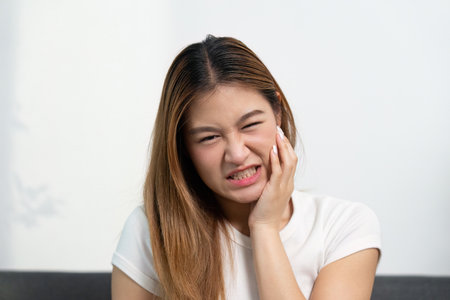 Toothache and Facial Discomfort. Young woman grimacing in pain at home.の写真素材
