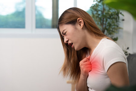 Chest Pain and Discomfort. Young woman holding her chest in distress at home.