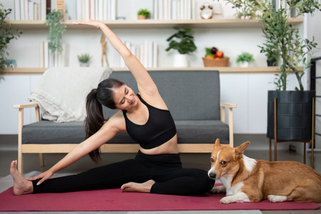Yoga Stretching with Pet. Woman practicing yoga beside her corgi dog at home.の写真素材