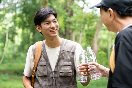 Father and Son Hiking Together. A joyful moment between a father and son sharing water in a lush forest.の写真素材