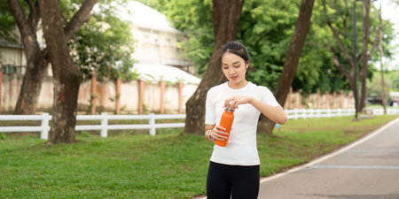 Active Lifestyle and Hydration. Young woman opening orange water bottle while walking in park.