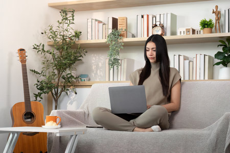 Remote Work and Digital Connection. Young woman using laptop at home for productivity.の写真素材
