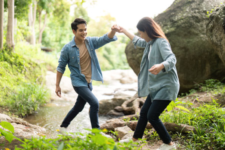 Couple enjoying playful moment while crossing stream. Young man and woman holding hands in nature.の写真素材