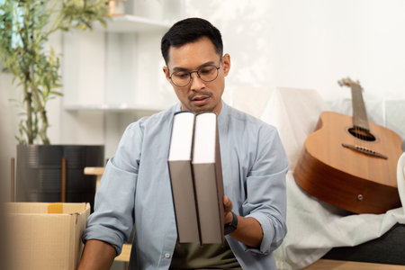 Gay man examining books while unpacking in a new homeの写真素材