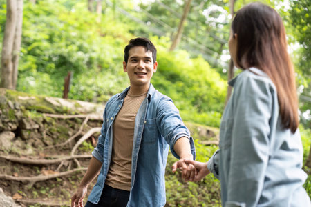 Couple enjoying playful moment in nature. Young man and woman holding hands while exploring a lush...
