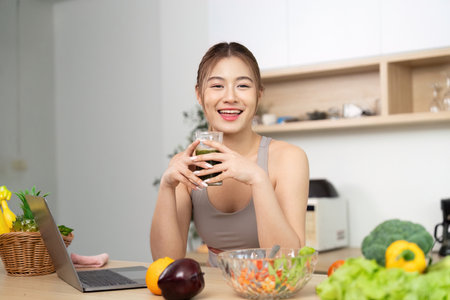 Wellness and Nutrition. Smiling woman enjoying green smoothie at home with laptop.の写真素材