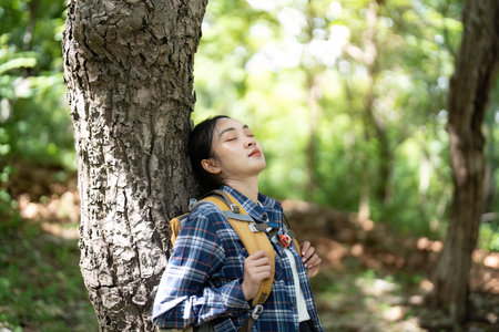 Relaxation in Nature. Young woman resting against a tree in a serene forest.の写真素材