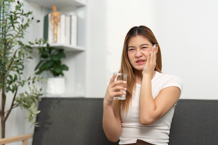 Health Awareness: Young woman holding a glass of water, showing discomfort.の写真素材
