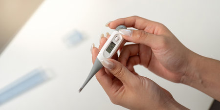 Health Monitoring. Woman checking temperature with digital thermometer at home.の写真素材