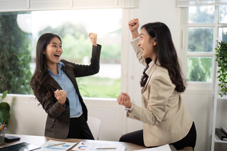 Excitement in the Office. Two businesswomen celebrating a win with raised fists.