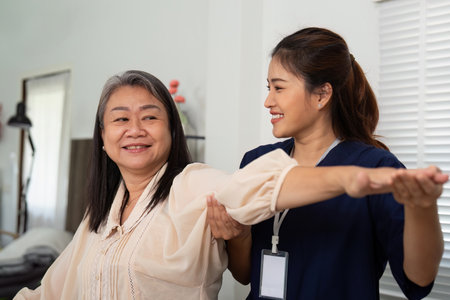 Caregiver encouraging elderly woman during mobility exercise at homeの写真素材