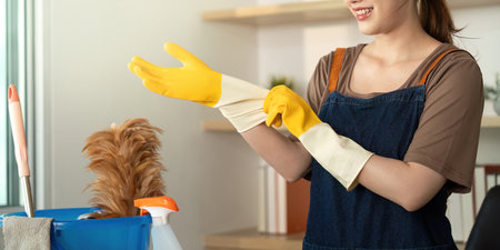 Home Cleaning. Woman wearing yellow gloves preparing for cleaning tasks in a modern workspace.