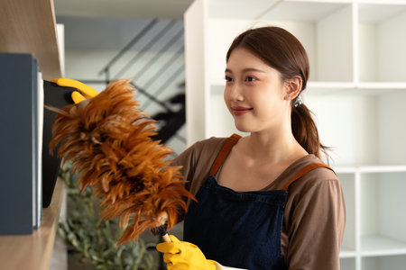 Home Cleaning. Young woman dusting shelf with feather duster and smile.の写真素材