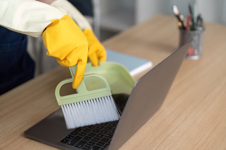 Cleaning Technology. Person using a brush and dustpan to maintain laptop hygiene.