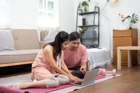 Couple working on a laptop together, planning fitness goals at homeの写真素材