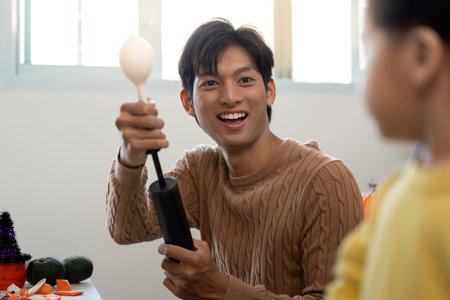 Joyful Halloween Preparation. A young man shares a fun moment with a child while crafting.