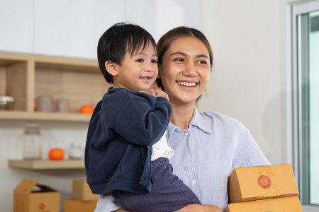 Family Business. A mother joyfully carries her child while managing packages.の写真素材