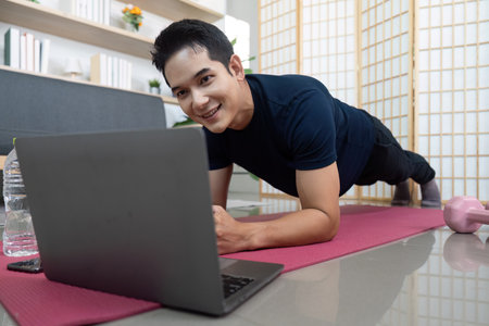 Man performing plank exercise while using laptop at homeの写真素材