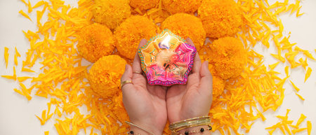 Diwali Ritual. Colorful diya held above marigold flowers for festive celebration.
