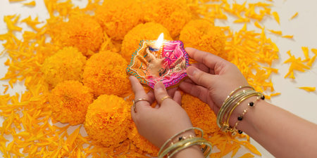 Diwali Celebration. Hands holding traditional diya surrounded by marigold flowers.