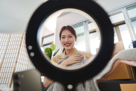 Online Shopping. Woman smiling while displaying a sweater through a ring light.
