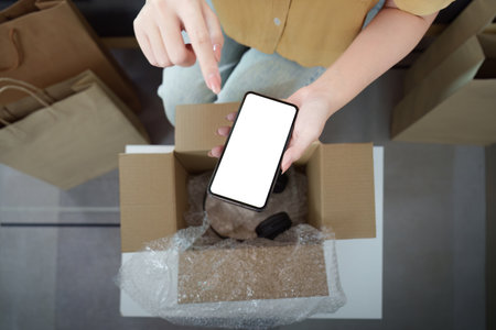 Online shopping. Unboxing a delivery with smartphone in hand.
