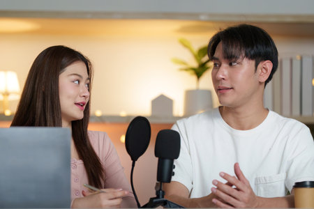 Podcasting duo. Engaging conversation between two young adults in a cozy studio.の写真素材