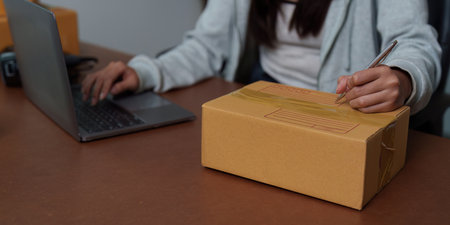 E-commerce: Individual labeling packages while using a laptopの写真素材