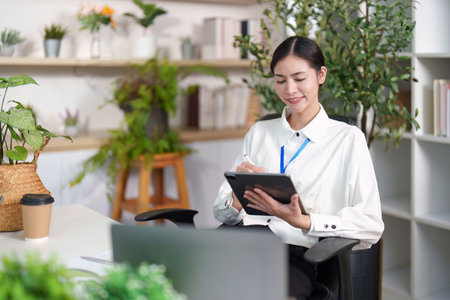 Smiling woman taking notes on tablet in modern workspaceの写真素材