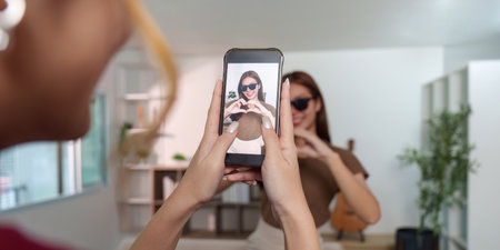 Creative Capture. Young woman posing for a smartphone photo while making a heart gesture.の写真素材