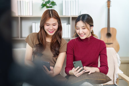 Friendship Moments. Two young women sharing laughter while using smartphones.の写真素材