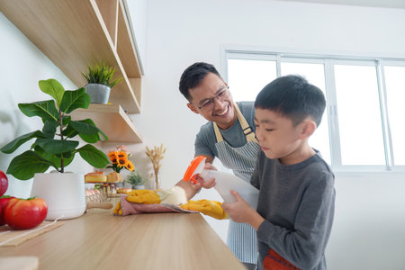 Home Cleaning. Father teaching son to clean kitchen surfaces.