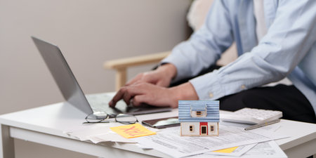Home Ownership. Man typing on laptop with house model and tax documents on table.の写真素材
