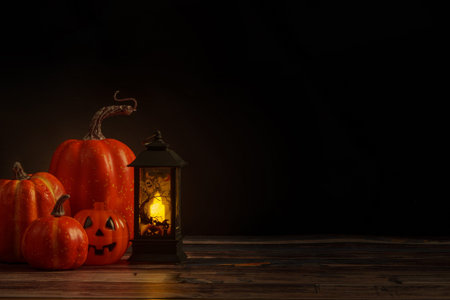 Halloween pumpkins and lit lantern on wooden table with dark background