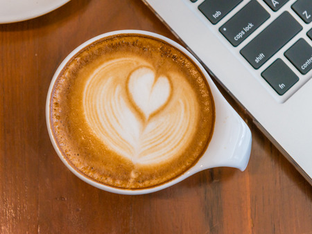 Laptop and hot cup of coffee on wood table, business conceptの写真素材