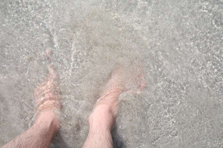 Man's feet in the sea water. View from above. Copy space.